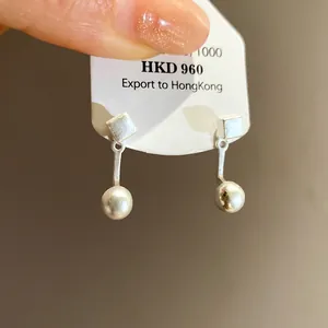 Dettaglio di orecchini pendenti minimalisti in argento su cartoncino bianco export
