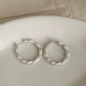 Primer plano detallado de aretes de aro plateados con textura esmerilada girada