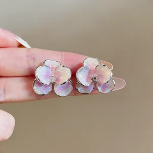 Dettaglio di orecchini a lobo a forma di fiore con smalto glitterato e zircone centrale