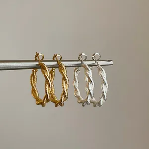 Vista detallada de pendientes de aro de metal trenzado con un acabado mate dorado y plateado
