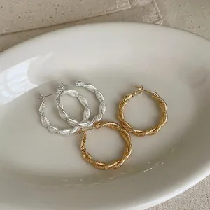 Primer plano de pendientes de aro de metal trenzado con textura mate y acabado brillante.