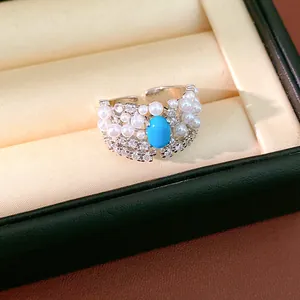 Macro view of an elegant vintage ring featuring turquoise, white pearls, and sparkling zircons.