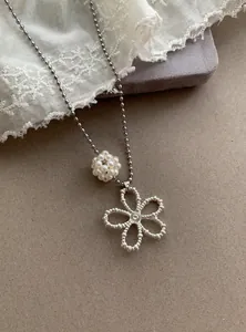 Close-up of a decorative pearl bead and textured hollow flower pendant on silver bead chain
