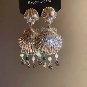 Primer plano de pendientes de concha dorada con borlas de cuentas y textura metálica.