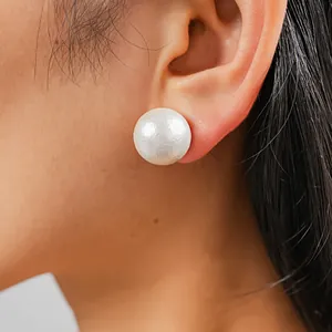 Primo piano di un singolo orecchino a perla bianca oversize sull'orecchio di un modello