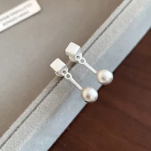 Primo piano degli orecchini a pendente in argento S925 con design a cubo e sfera.