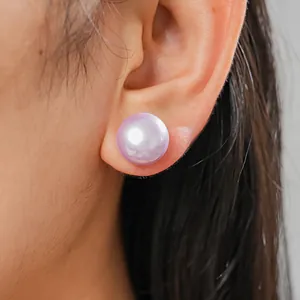 Primo piano di un orecchino a bottone con perla sintetica viola indossato sull'orecchio.