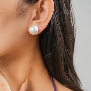 Primo piano di un grande orecchino a perno con perla bianca indossato da una modella