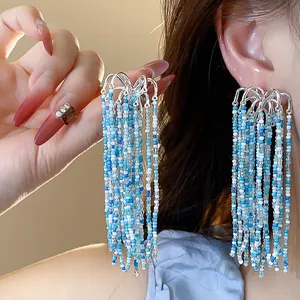 Detail view of handcrafted blue and white glass bead tassel earrings worn on ear.