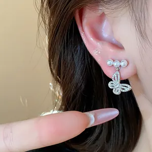 Close-up view of silver hollow butterfly earrings with sparkling pearls worn on an ear