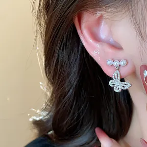 Elegant detail of a silver butterfly earring with small pearls worn on a human ear