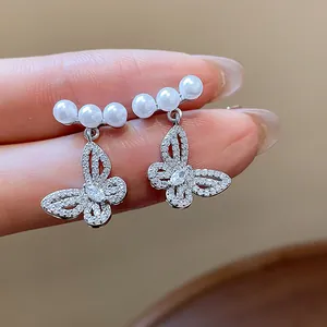 Close-up of hollow butterfly stud earrings with white pearls, held by fingers for detail.