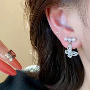 Detail view of silver butterfly pearl stud earrings with sparkling crystals on ear