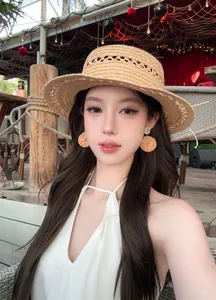Gros plan de boucles d'oreilles rondes en paille tressée bohème sur un mannequin à la plage.