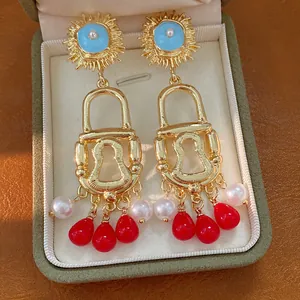 Detailed view of gold lock earrings with blue sun motif and red pearl tassels