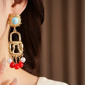 Detail view of exaggerated gold lock earrings with red beads and pearls on model.