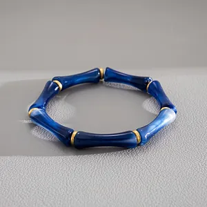Dettaglio di un bracciale elastico in acrilico blu con design a bambù e distanziatori oro.