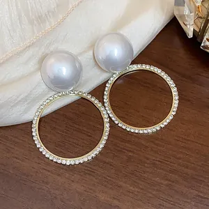 Detalle de pendientes de perlas redondas con un aro dorado de pedrería brillante.