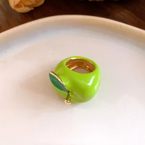 Primer plano de un anillo de manzana en esmalte verde brillante con detalle dorado.