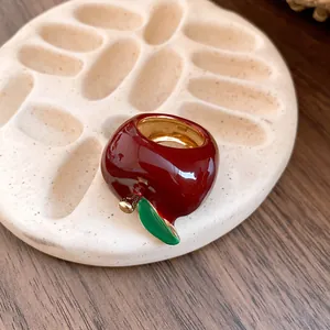 Primer plano de un anillo con forma de manzana en esmalte rojo brillante y hoja verde.