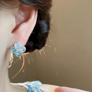 Detailed close-up of a silver four-leaf clover earring with light blue zircon stones.