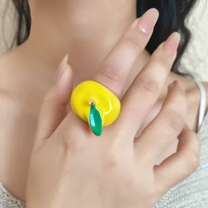 Primer plano de un anillo de manzana de esmalte amarillo de estilo francés en un dedo