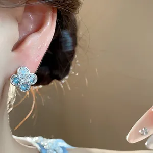Detailed close-up of a delicate silver flower earring with blue zircon stones on an ear