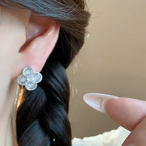 Detail shot of a silver four-leaf clover earring with white stones on a model's ear