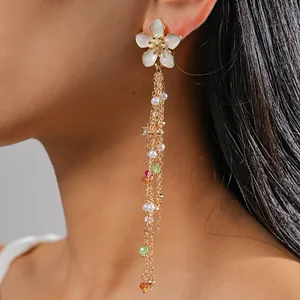 Detail view of long gold tassel earring with white flower stud and colorful beads on ear
