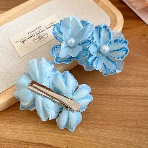 Detail view of blue fabric flower hair clip with pearl and silver alligator clip back.