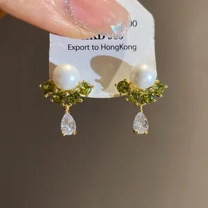 Detailed view of elegant 14k gold plated earrings with pearls and green zircons.