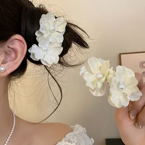 Detail showing elegant fabric flower hair clips with pearl centers on hair and hand.
