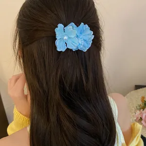 Elegant blue fabric flower hair clip with pearl detail worn on styled long brown hair