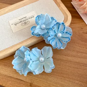 Close-up detail of blue fabric flower hair clips with pearl centers on a wooden tray