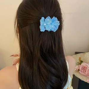 Close-up of a blue fabric flower hair clip with a pearl center worn in long hair