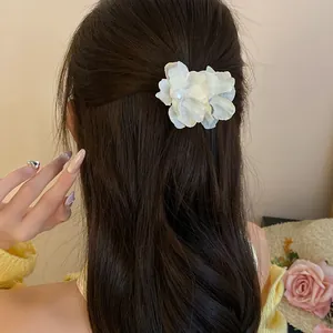 Close-up detail of a white fabric flower hair clip with pearl center on dark hair