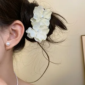 Close-up of white fabric flower hair clip with pearl center worn on model's hair.