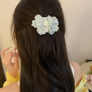 Detail view of a sweet fabric flower hair clip with pearl centers on model's dark hair