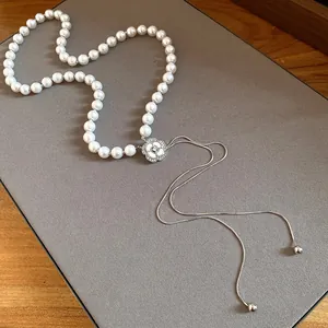 Detail shot of a white pearl necklace with a rhinestone flower pendant and tassels.