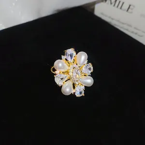 Detailed macro shot of a flower-shaped zircon and pearl open ring on black velvet.