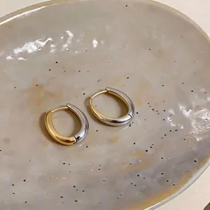 Primo piano di orecchini a cerchio ovali bicolore oro e argento su base ceramica