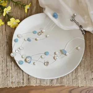 Dettaglio macro della collana multistrato minimalista con perle bianche e pietre blu su piatto