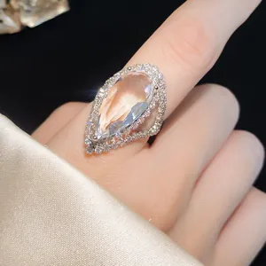 Close-up of elegant teardrop-cut zircon ring on finger with luxury silk background.