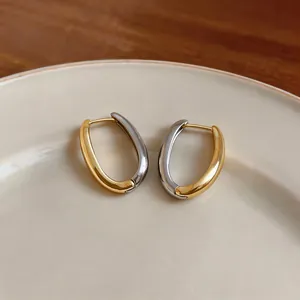 Dettaglio di orecchini a cerchio ovali bicolore oro e argento su un piatto in ceramica