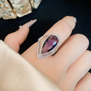 Detailed view of a large pear-shaped purple zircon ring with a diamond-like halo on a finger