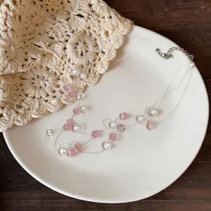 Dettaglio di collana multistrato con pietre rosa e perle bianche su un piatto crema