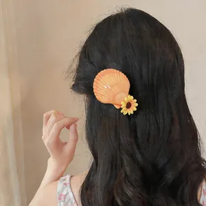 Détail d'une pince à cheveux coquillage orange et fleur jaune sur cheveux noirs ondulés