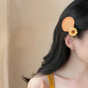 Détail d'une pince à cheveux coquillage et tournesol sur de longs cheveux.