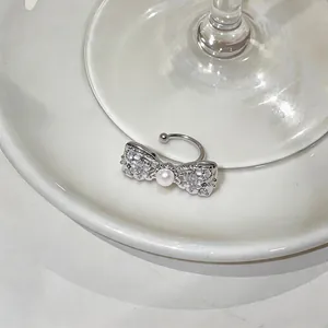 Macro view of a silver bow ear cuff featuring sparkling zircons and a white pearl
