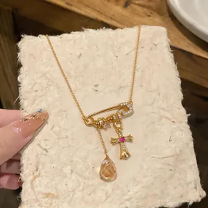 Detail view of 18k gold plated safety pin necklace with cross charm and crystal teardrop